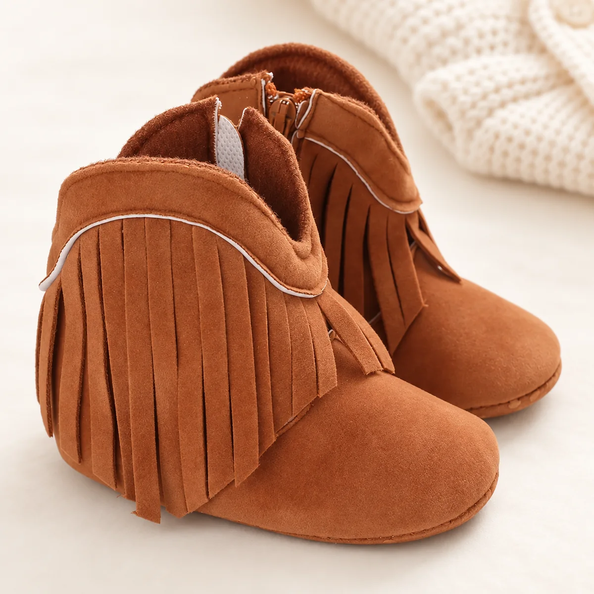 Bottines bébé marron à franges sur un fond clair avec une maille écrue