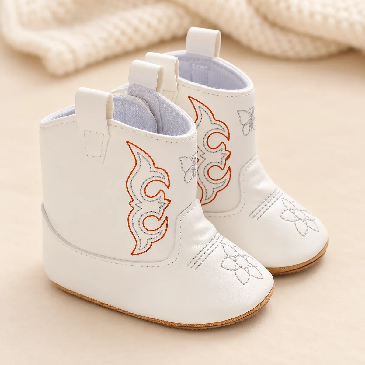 Bottines bébé western blanches brodées sur un fond clair avec une maille écrue