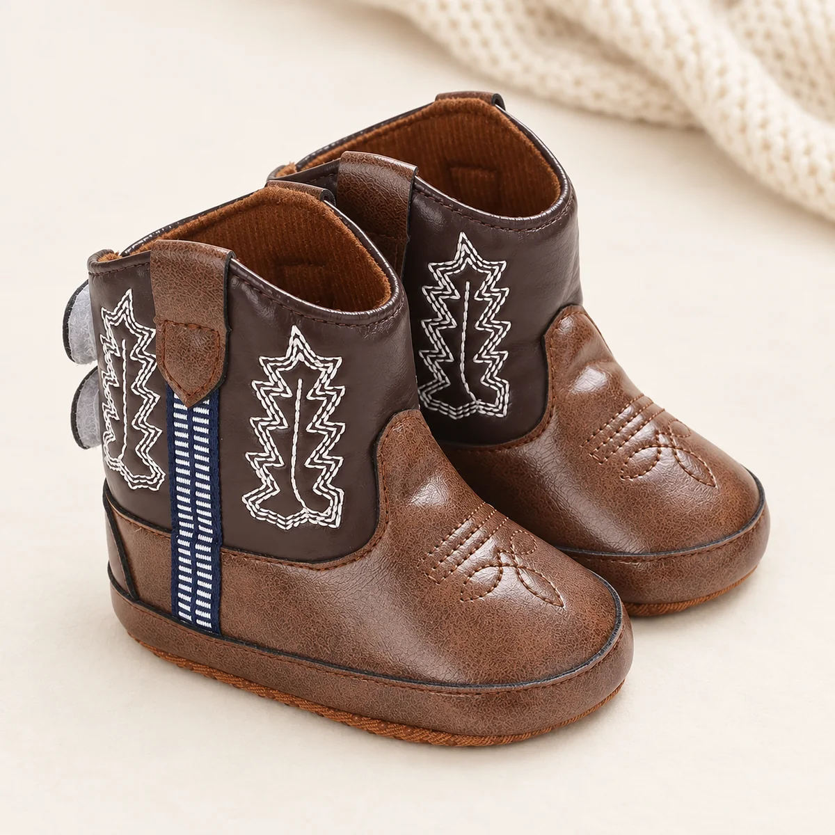 Bottines bébé western marron à feuille brodée sur un fond clair avec une maille écrue