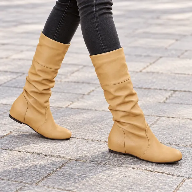 Bottes femme beige sable plissées à enfiler, portées en marchant avec un pantalon sombre