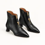 Bottines noires pour femme à bout pointu avec zip doré sur fond blanc
